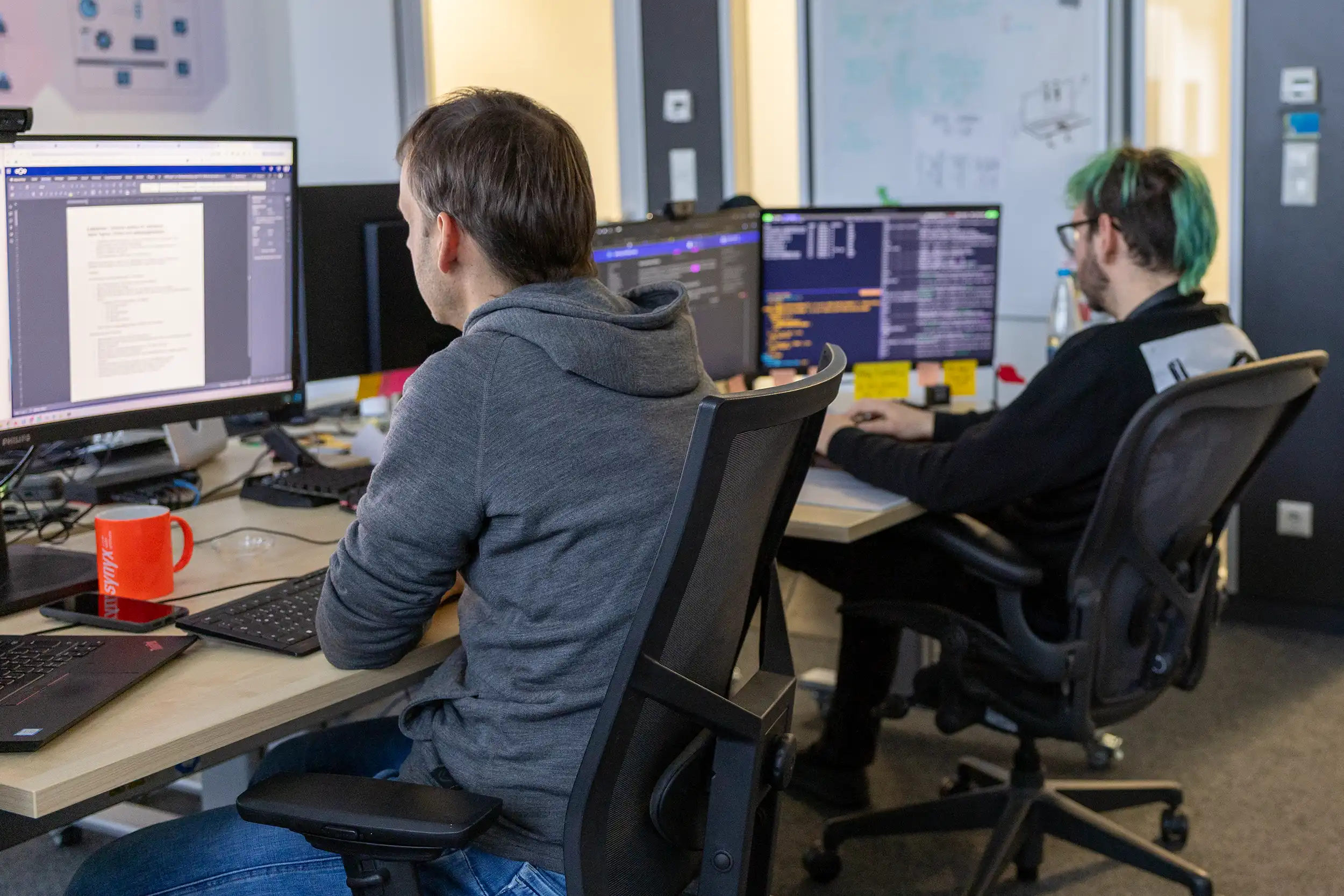 Entwickler programmiert an drei Bildschirmen mit ergonomischer Split-Tastatur.